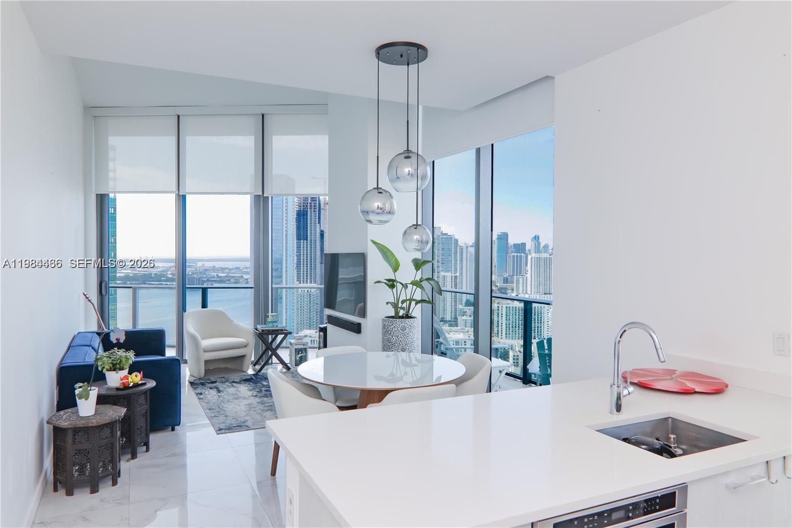 A modern apartment living and dining area features floor-to-ceiling windows with city and water views — 501 NE 31st St # 4008, Miami FL 33137, MIAMI, FL