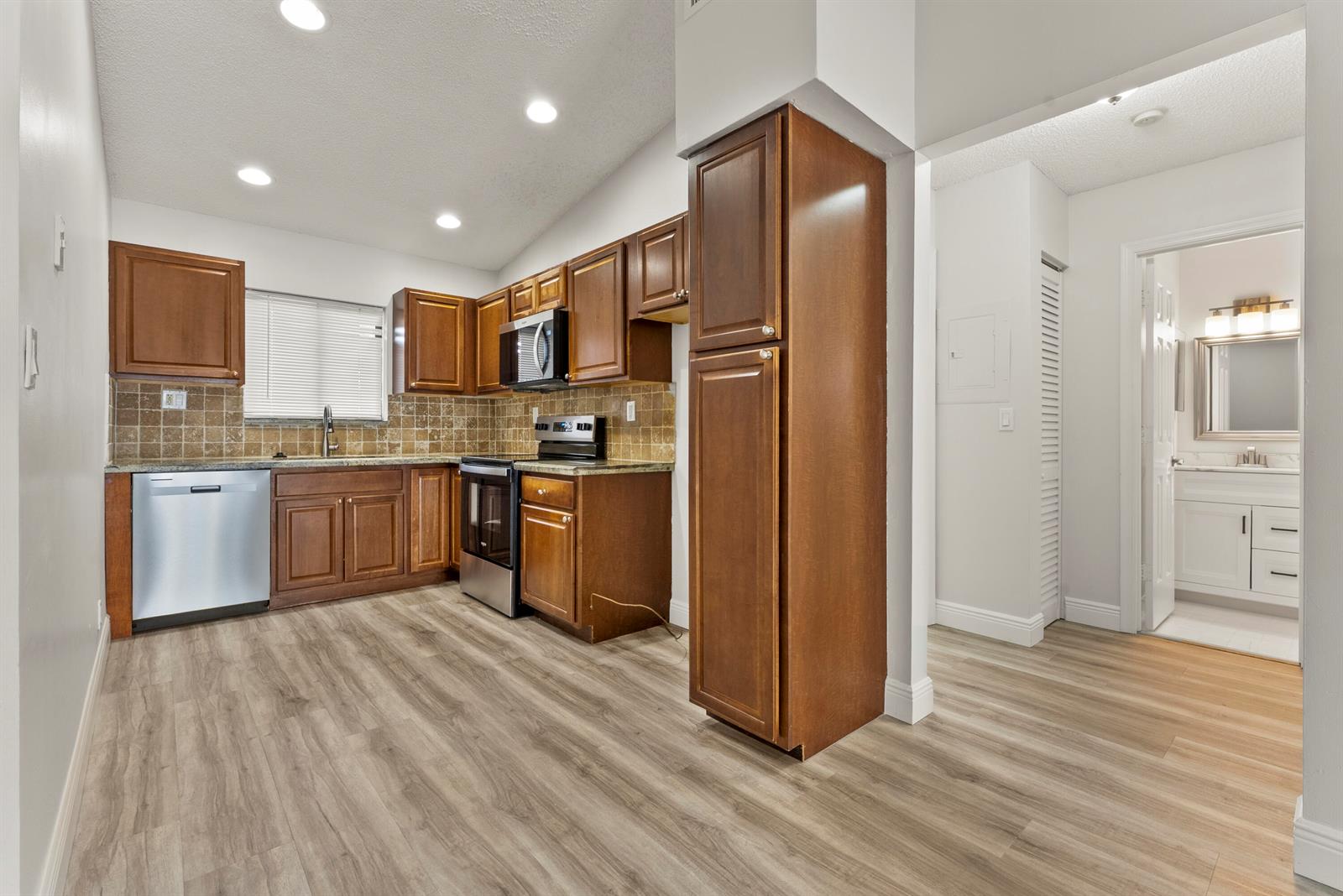 A kitchen with wood cabinets, stainless steel appliances, and wood-look flooring leads to a bathroom — 2900 Olivewood Terrace # 201, Boca Raton FL 33431, BOCA RATON, FL