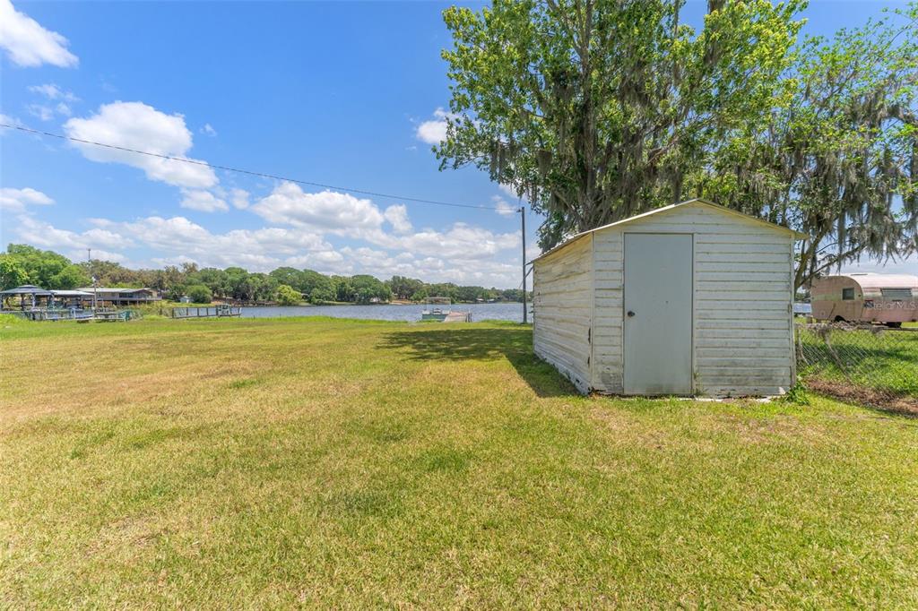 A white storage shed sits on a grassy lawn overlooking a lake with a dock — 7558 BERKLEY ROAD, POLK CITY, FL