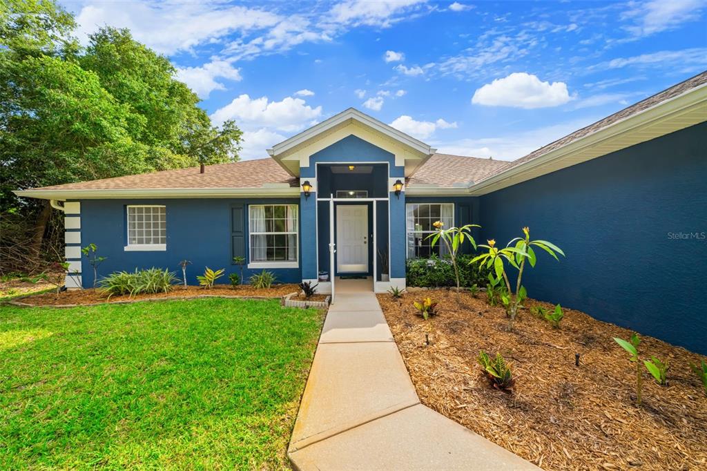 A blue single-story house features a white front door, a concrete walkway, and landscaped mulch — 3254 WASILLA AVENUE SE, PALM BAY, FL