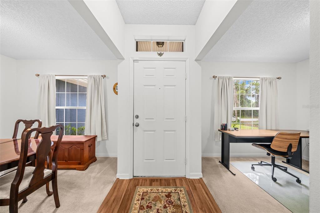 An entryway features a white front door, wood-look flooring, and carpeted dining and office areas — 3254 WASILLA AVENUE SE, PALM BAY, FL