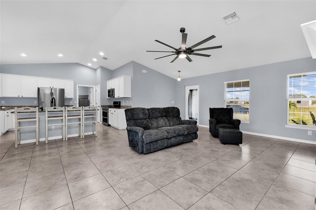 An open-concept living room and kitchen with white cabinets, tile flooring, and vaulted ceilings — 2926 NW 25TH STREET, CAPE CORAL, FL