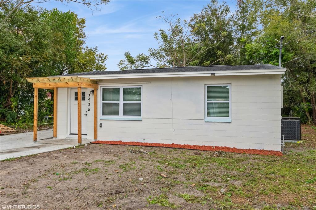 A single-story white concrete block house features a wooden pergola over the front entrance — 3935 WELLS STREET, ORLANDO, FL