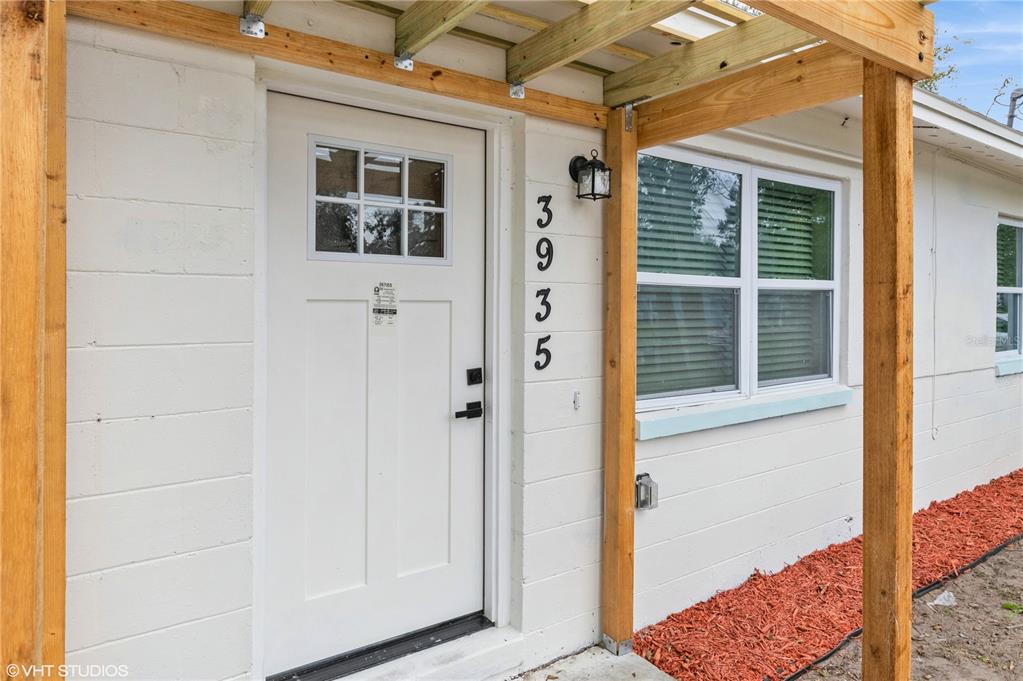 A white exterior wall features a front door, a window, and a wooden pergola structure — 3935 WELLS STREET, ORLANDO, FL