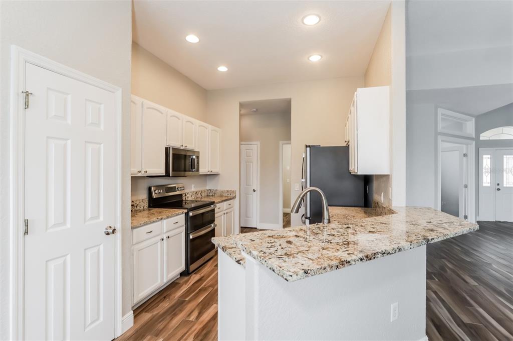 A kitchen features white cabinets, granite countertops, stainless steel appliances, and wood-look flooring — 2954 DUNHILL CIRCLE, LAKELAND, FL