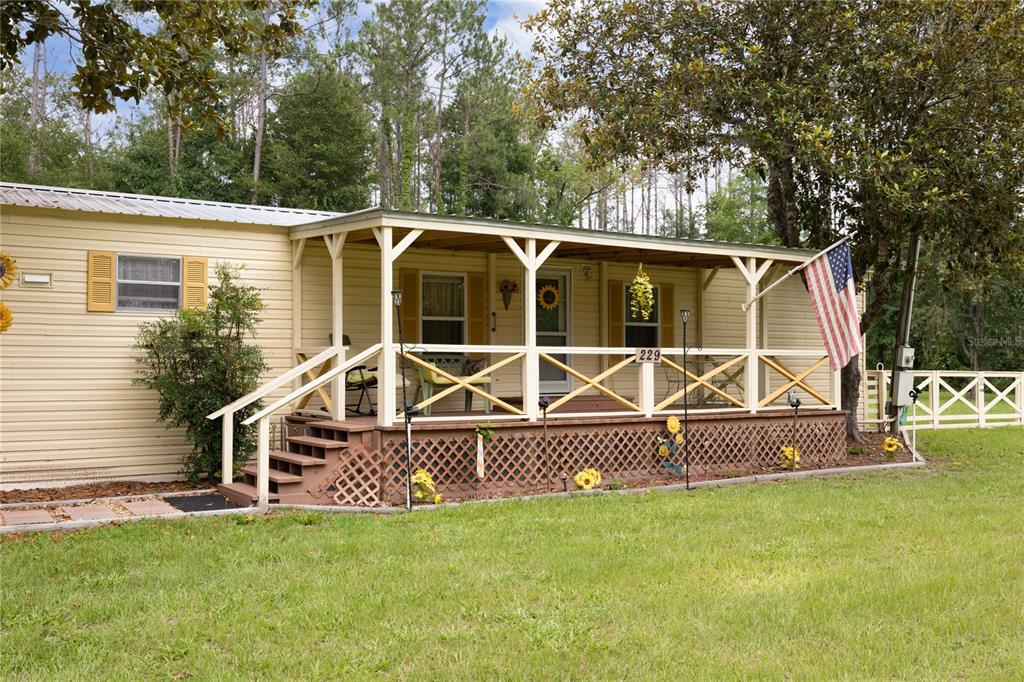 A light-colored manufactured home features a covered wooden front porch with lattice skirting — 229 SW BARWICK TERRACE, LAKE CITY, FL