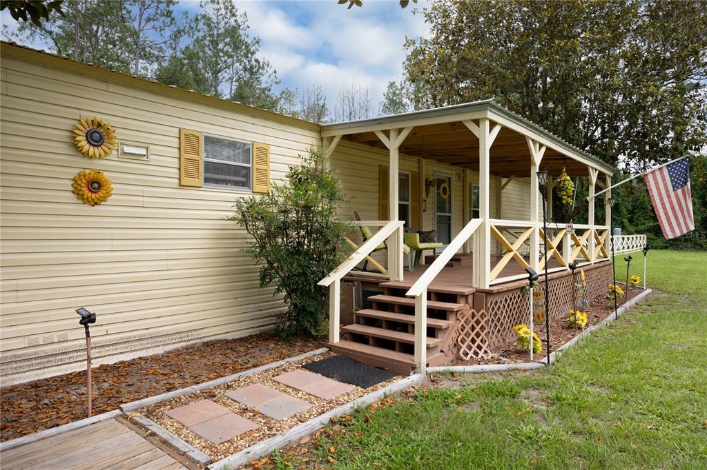 A beige mobile home features a wooden front porch with stairs and a flag — 229 SW BARWICK TERRACE, LAKE CITY, FL