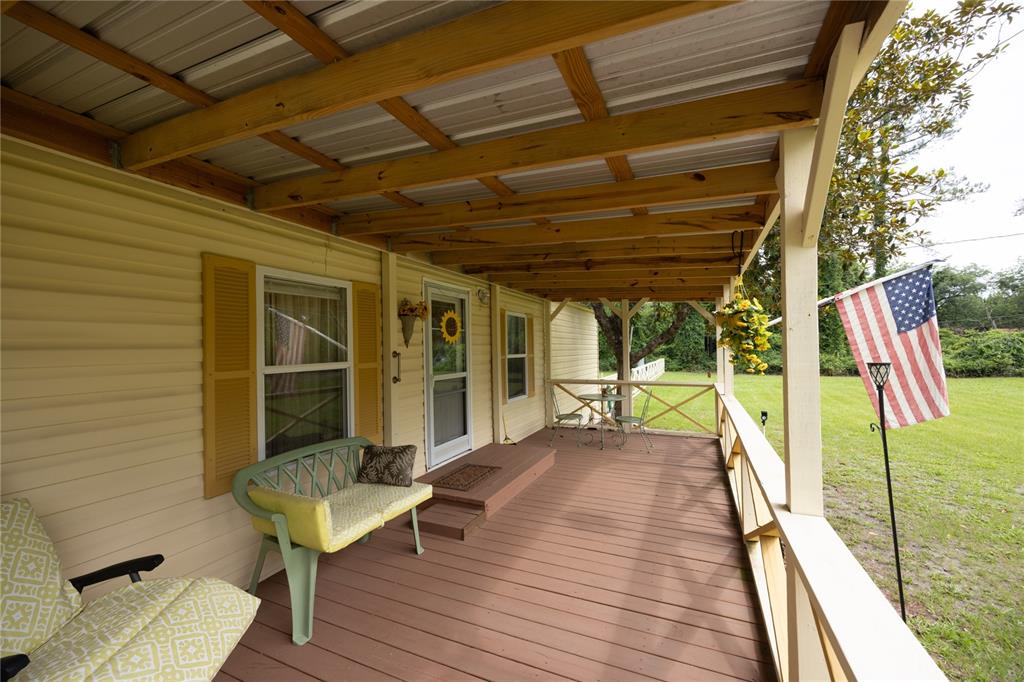 A covered wooden porch with a bench, table, chairs, and an American flag — 229 SW BARWICK TERRACE, LAKE CITY, FL