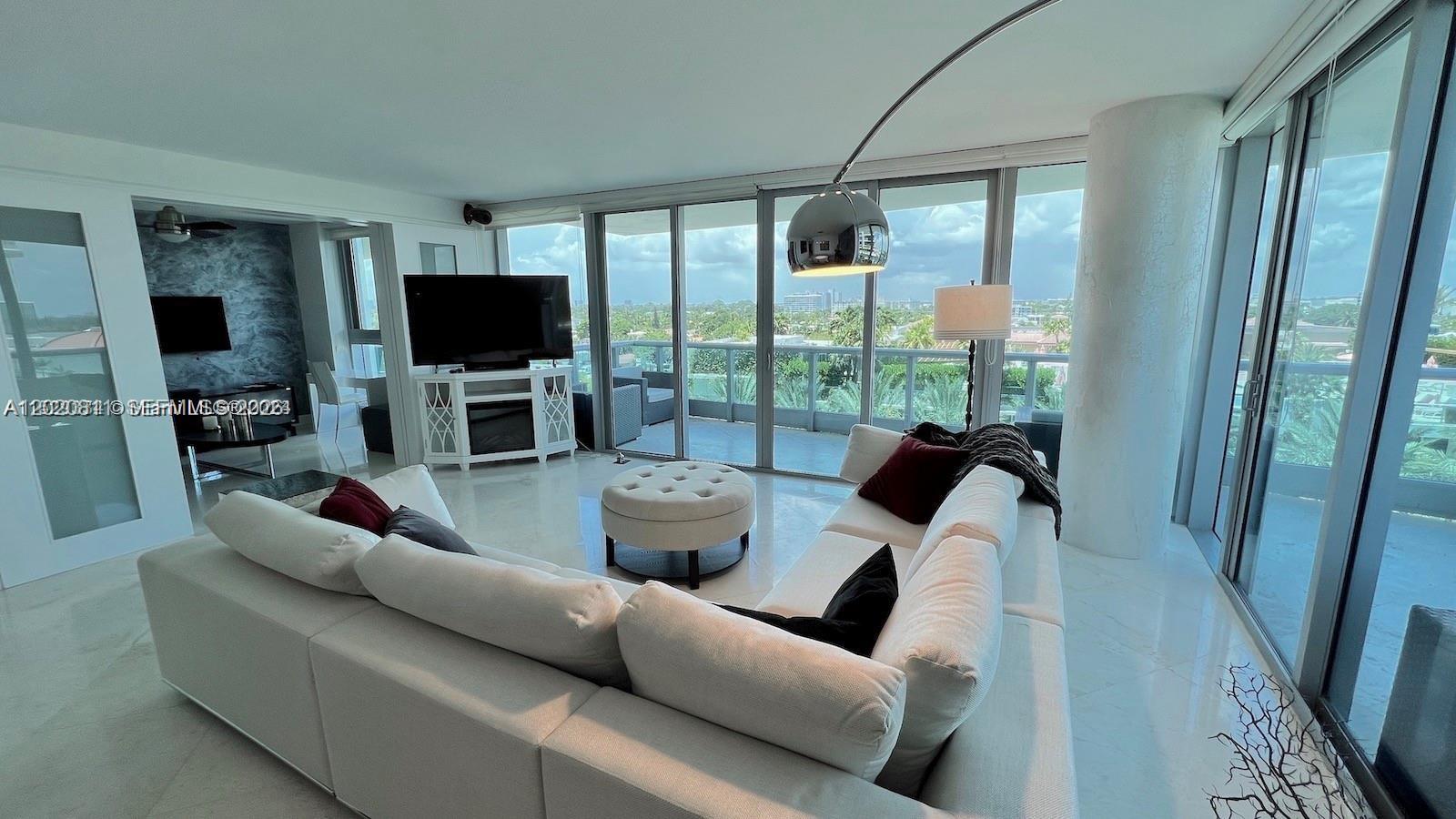 A modern living room features a white sectional sofa, a round ottoman, and floor-to-ceiling windows — 9401 Collins Ave # 603, Surfside FL 33154, SURFSIDE, FL