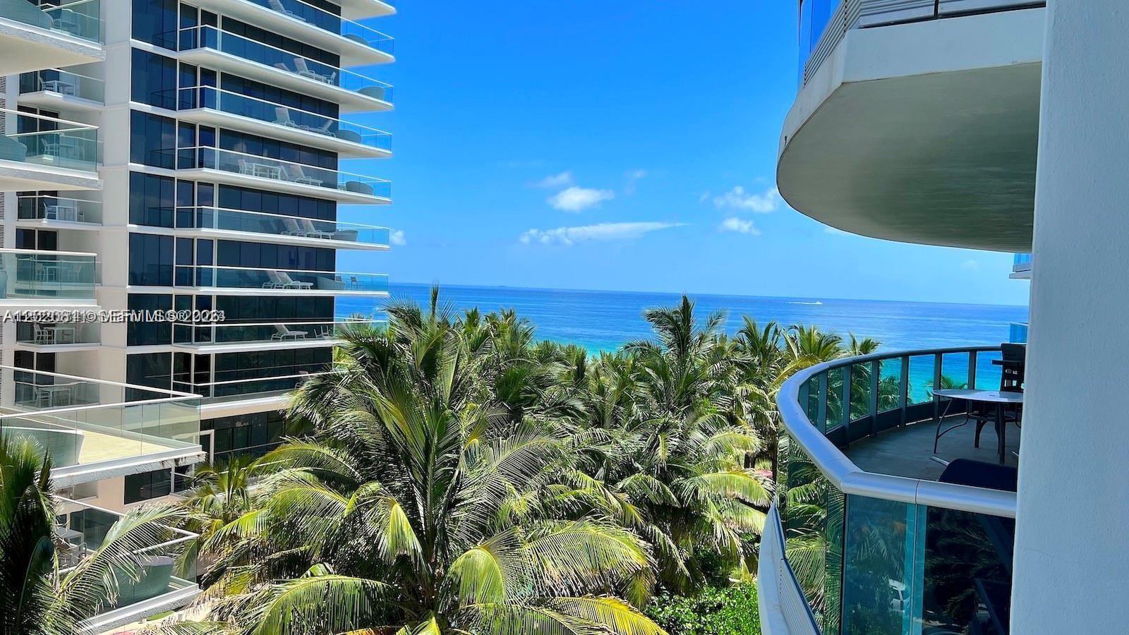 A view from a balcony overlooking palm trees and the ocean between two high-rise buildings — 9401 Collins Ave # 603, Surfside FL 33154, SURFSIDE, FL