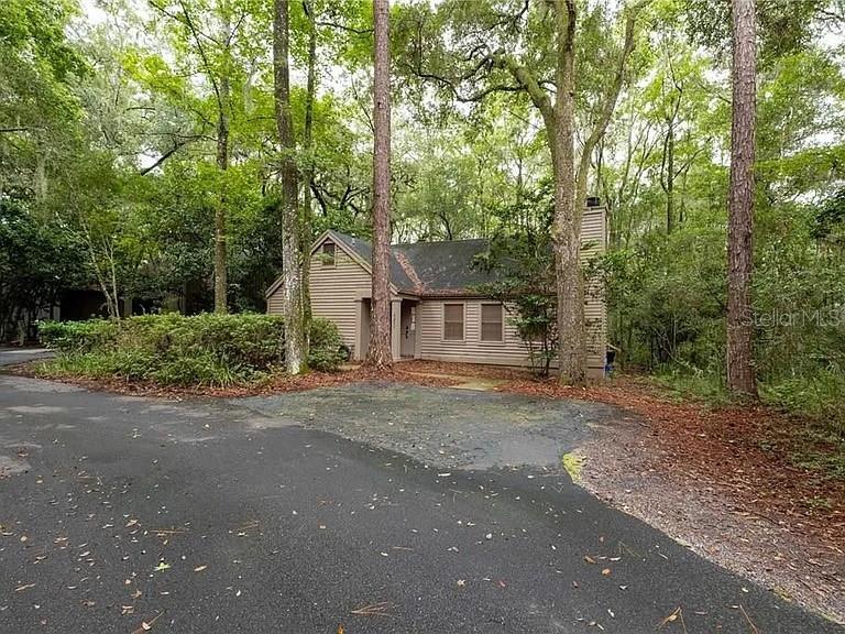 A tan-sided house with a dark roof sits in a wooded area near a driveway — 5211 SW 86TH TERRACE, GAINESVILLE, FL