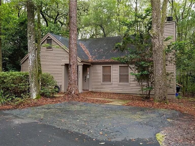 A brown, single-story house with horizontal siding is nestled among many tall trees — 5211 SW 86TH TERRACE, GAINESVILLE, FL