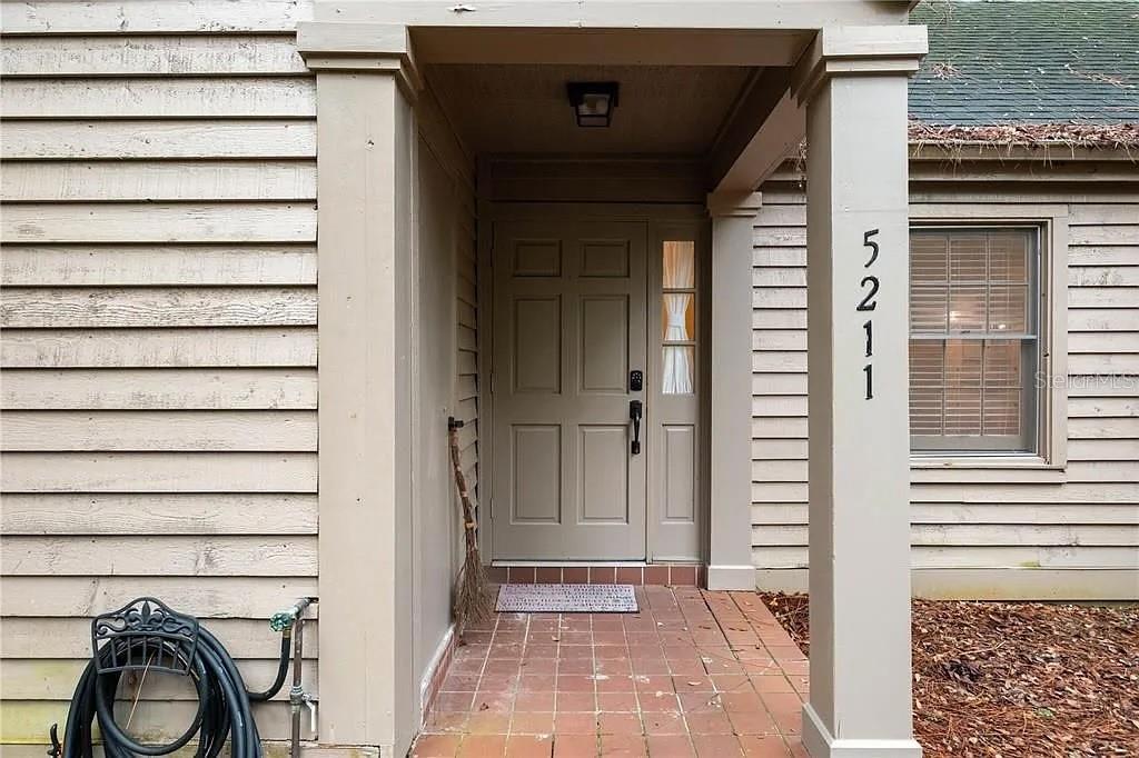 A beige front door with a side window is set under a covered porch entrance — 5211 SW 86TH TERRACE, GAINESVILLE, FL