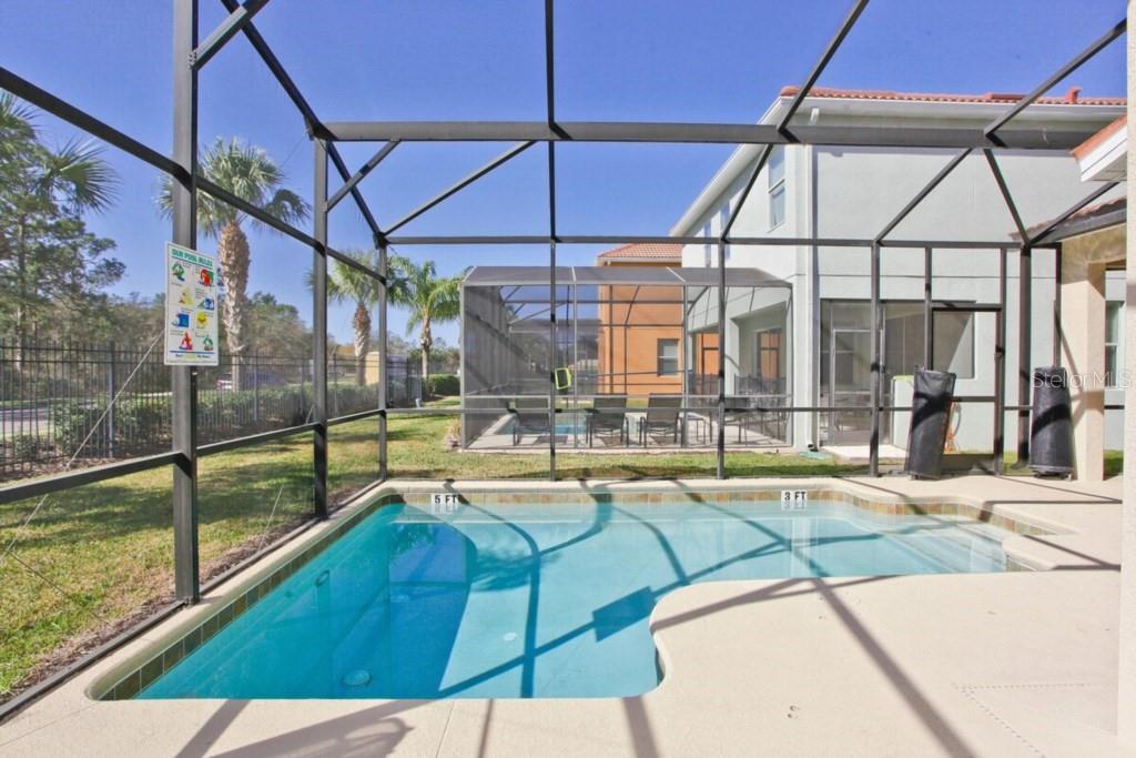 A swimming pool with a screen enclosure sits on a patio behind a two-story house — 8954 SUGAR PALM ROAD UNIT 8954, KISSIMMEE, FL