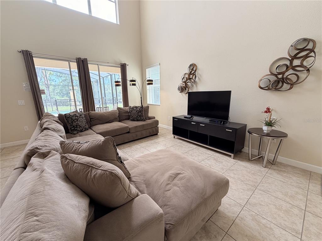 A living room features a large sectional sofa, a television on a stand, and tile flooring — 8954 SUGAR PALM ROAD UNIT 8954, KISSIMMEE, FL