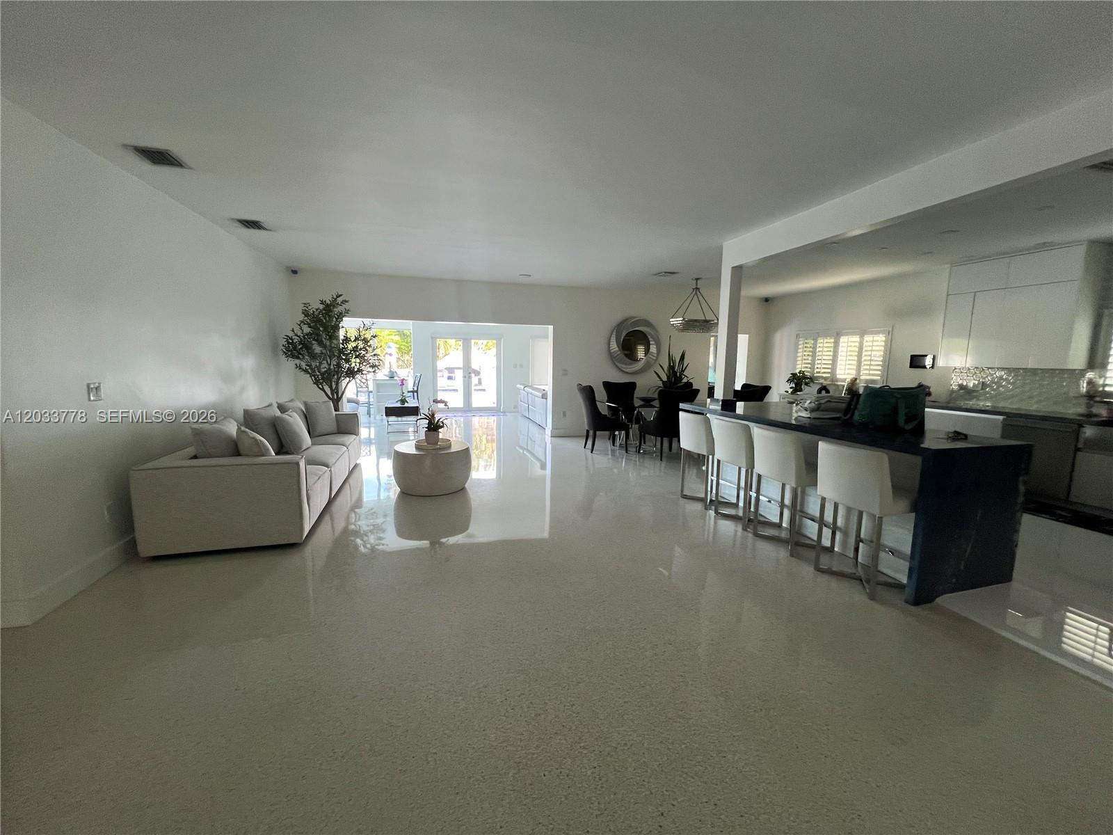 A spacious open-concept living area features white tile floors, a sofa, and a kitchen island — 1100 NE 84th St, Miami FL 33138, MIAMI, FL