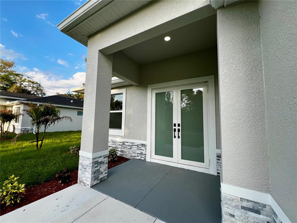 A covered entryway features a gray concrete floor, stone-accented columns, and double glass doors — 5126 CORNSILK TERRACE, NORTH PORT, FL