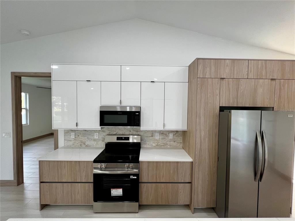 A kitchen features white upper cabinets, wood-grain lower cabinets, stainless steel appliances, and quartz countertops — 5126 CORNSILK TERRACE, NORTH PORT, FL