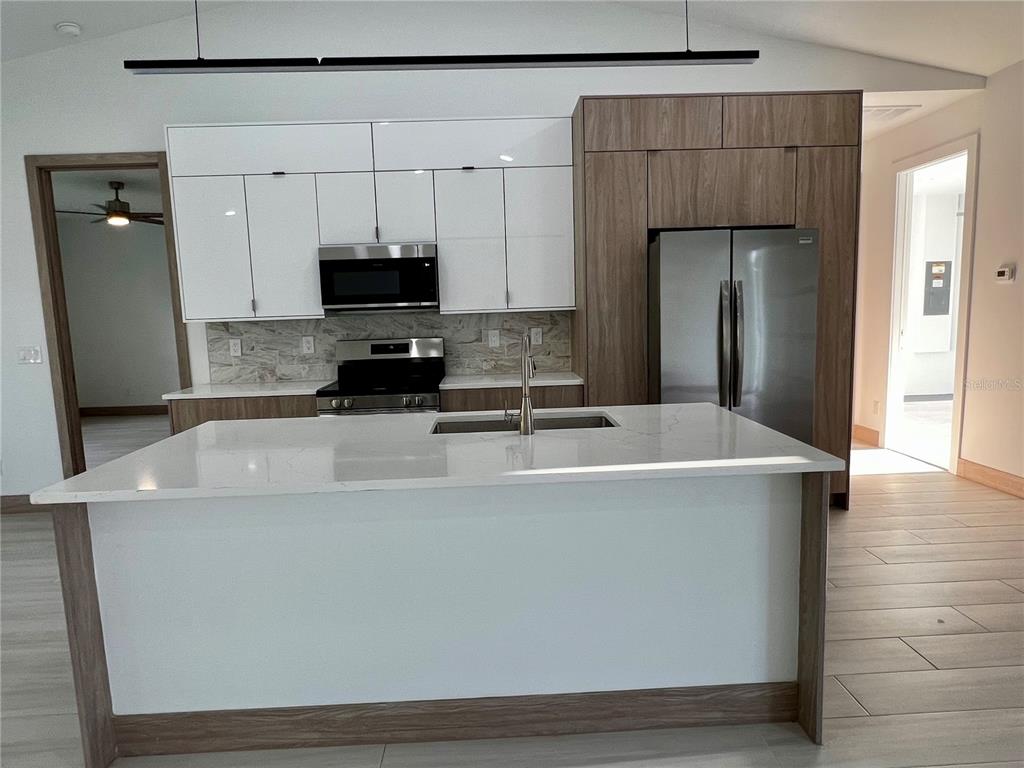 A modern kitchen features white upper cabinets, wood-tone lower cabinets, and a large central island — 5126 CORNSILK TERRACE, NORTH PORT, FL