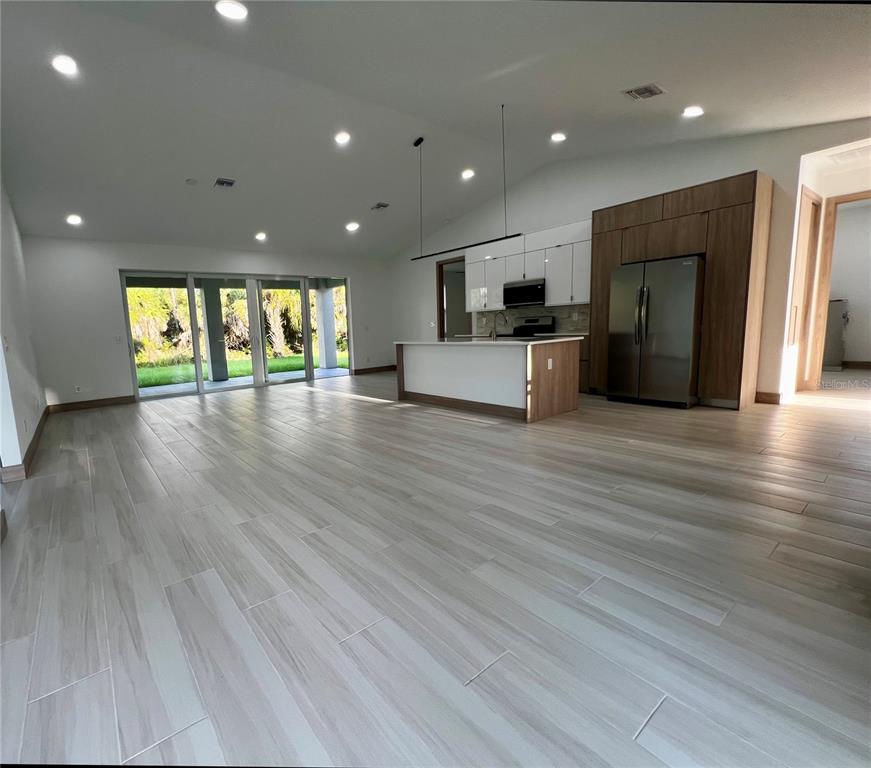 An open-concept kitchen and living area features light wood-look tile flooring and sliding glass doors — 5126 CORNSILK TERRACE, NORTH PORT, FL