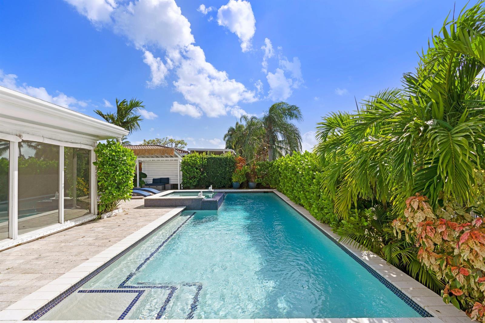 A rectangular swimming pool with an attached spa sits beside a house and tropical landscaping — 391 SE 7th Avenue, Pompano Beach FL 33060, POMPANO BEACH, FL