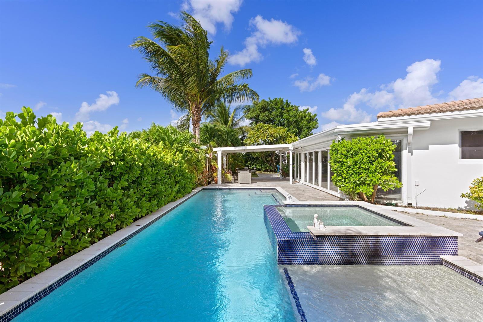 A rectangular swimming pool with an attached tiled spa sits beside a white house — 391 SE 7th Avenue, Pompano Beach FL 33060, POMPANO BEACH, FL