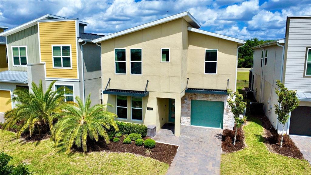 A two-story house with a tan stucco exterior, a green garage door, and palm trees — 2801 BOOKMARK DRIVE, KISSIMMEE, FL