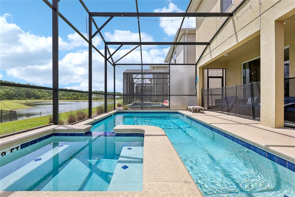 A screened-in pool and spa area overlooks a lake behind a residential home — 2801 BOOKMARK DRIVE, KISSIMMEE, FL