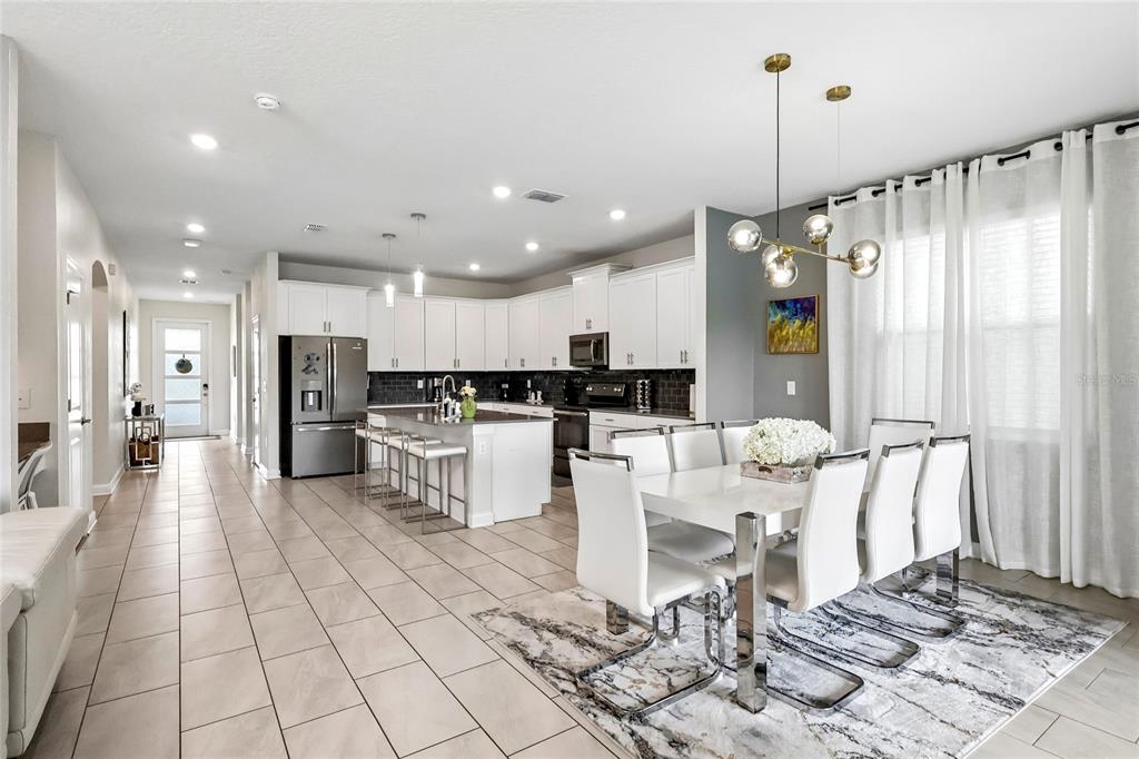 A bright open-concept kitchen and dining area with white cabinetry, tile floors, and modern lighting — 2801 BOOKMARK DRIVE, KISSIMMEE, FL