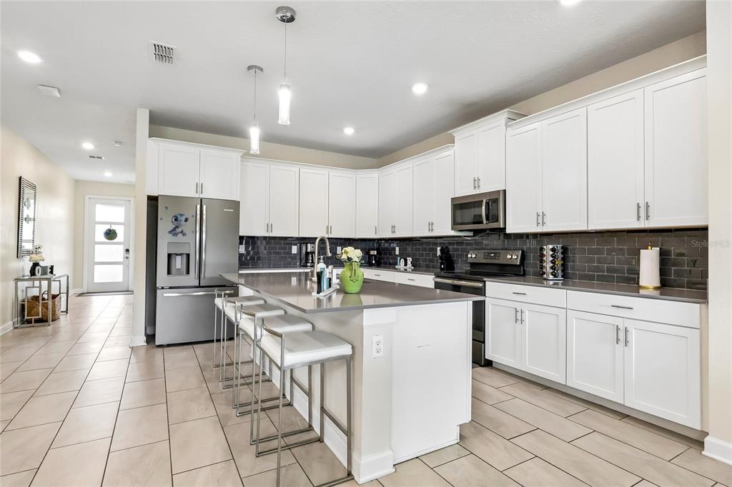 A modern kitchen features white cabinets, a gray island with bar stools, and dark tile backsplashes — 2801 BOOKMARK DRIVE, KISSIMMEE, FL