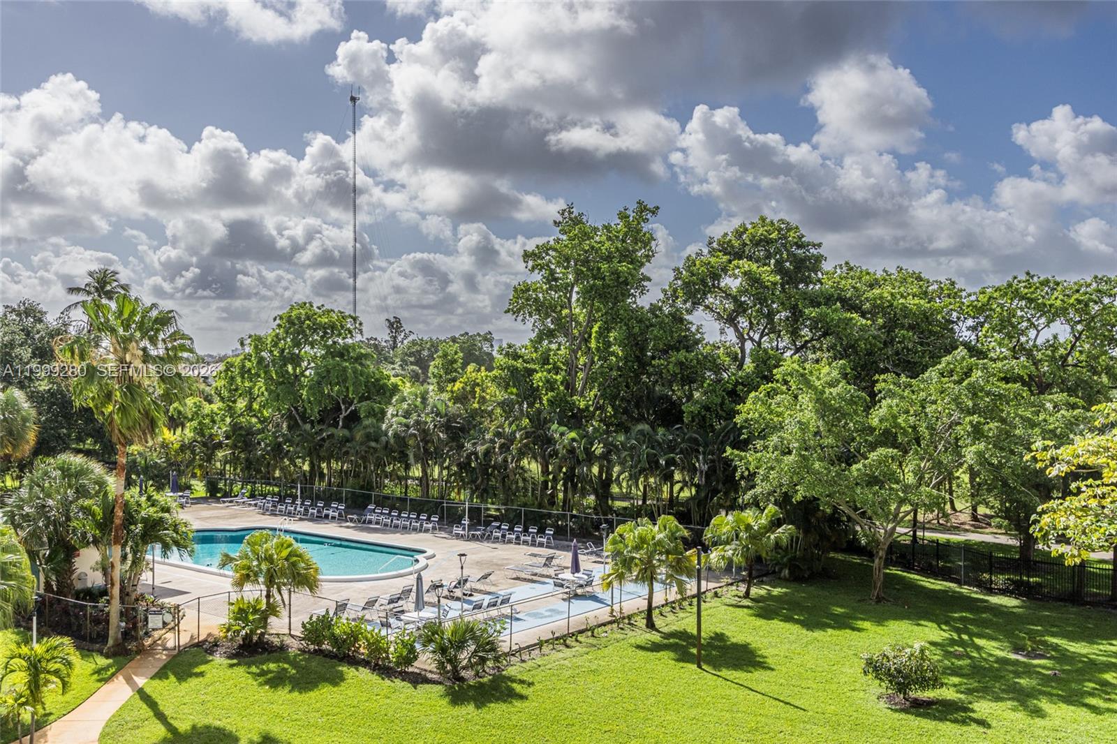 An outdoor swimming pool is surrounded by a patio, lounge chairs, and lush green trees — 4330 Hillcrest Dr # 405, Hollywood FL 33021, HOLLYWOOD, FL