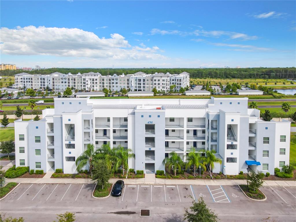 An aerial view of a multi-story apartment building with a parking lot in front — 4741 CLOCK TOWER DRIVE UNIT 107, KISSIMMEE, FL