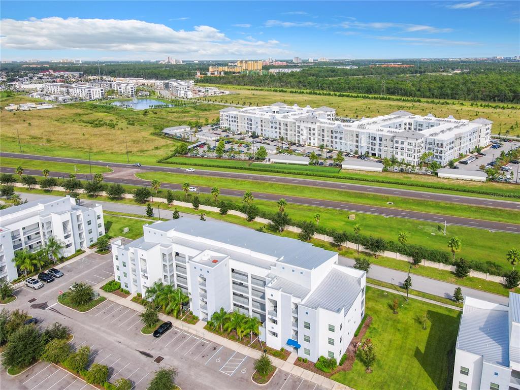 An aerial view shows multi-story apartment buildings surrounded by parking lots and grassy fields — 4741 CLOCK TOWER DRIVE UNIT 107, KISSIMMEE, FL