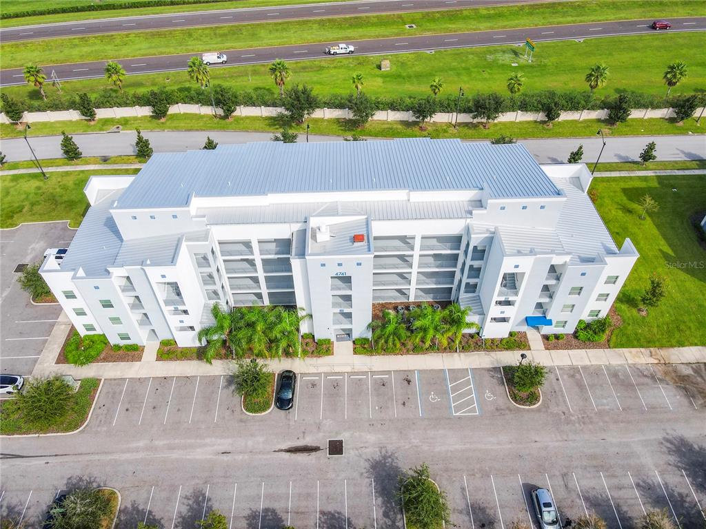 An aerial view shows a multi-story white building with a metal roof and parking lot — 4741 CLOCK TOWER DRIVE UNIT 107, KISSIMMEE, FL