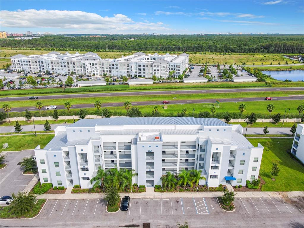 An aerial view shows a multi-story apartment building with a parking lot in front — 4741 CLOCK TOWER DRIVE UNIT 107, KISSIMMEE, FL