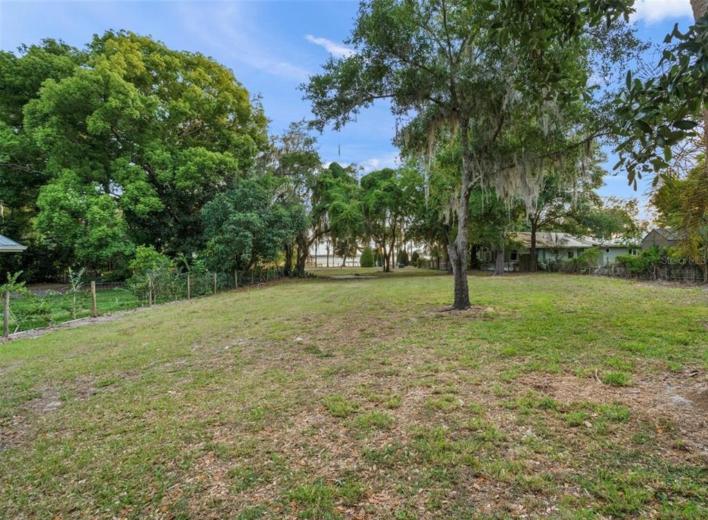 A grassy, tree-lined backyard lot with a fence and a view of water in the distance — LAKE LOUISA ROAD, CLERMONT, FL