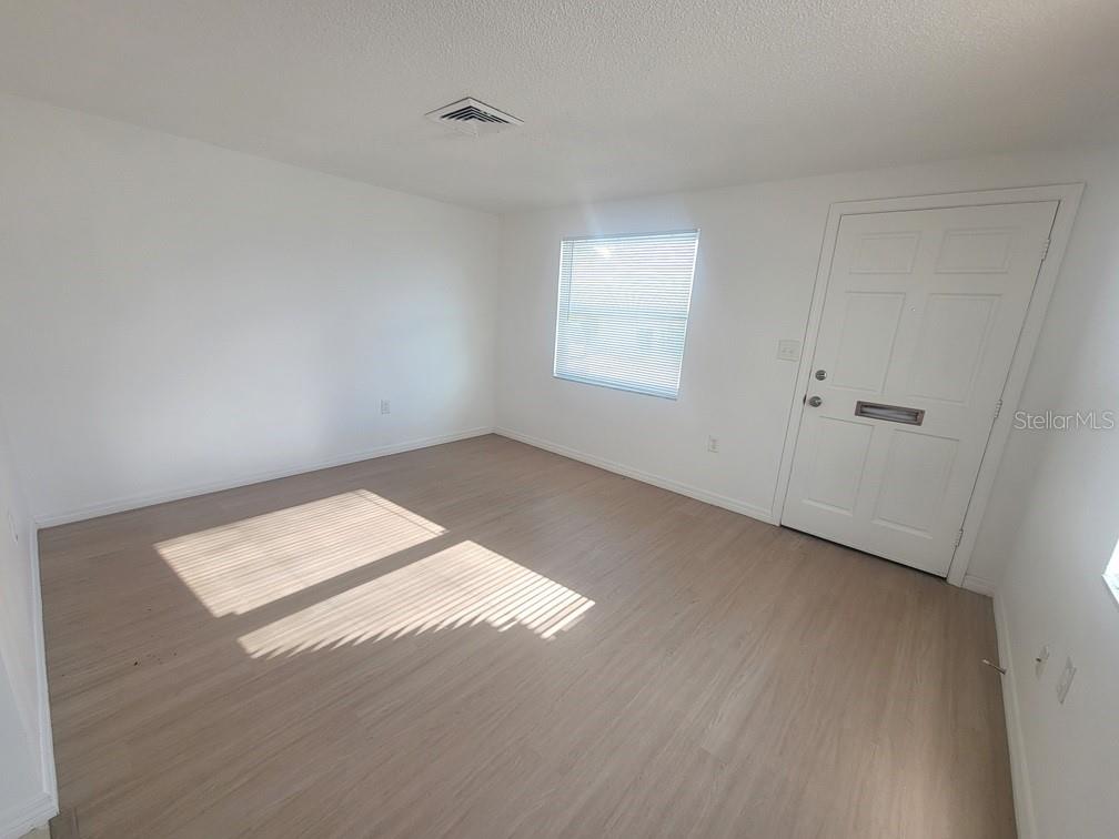 An empty room features light wood-look flooring, white walls, a window with blinds, and a door — 4922 FILNER STREET, NEW PORT RICHEY, FL