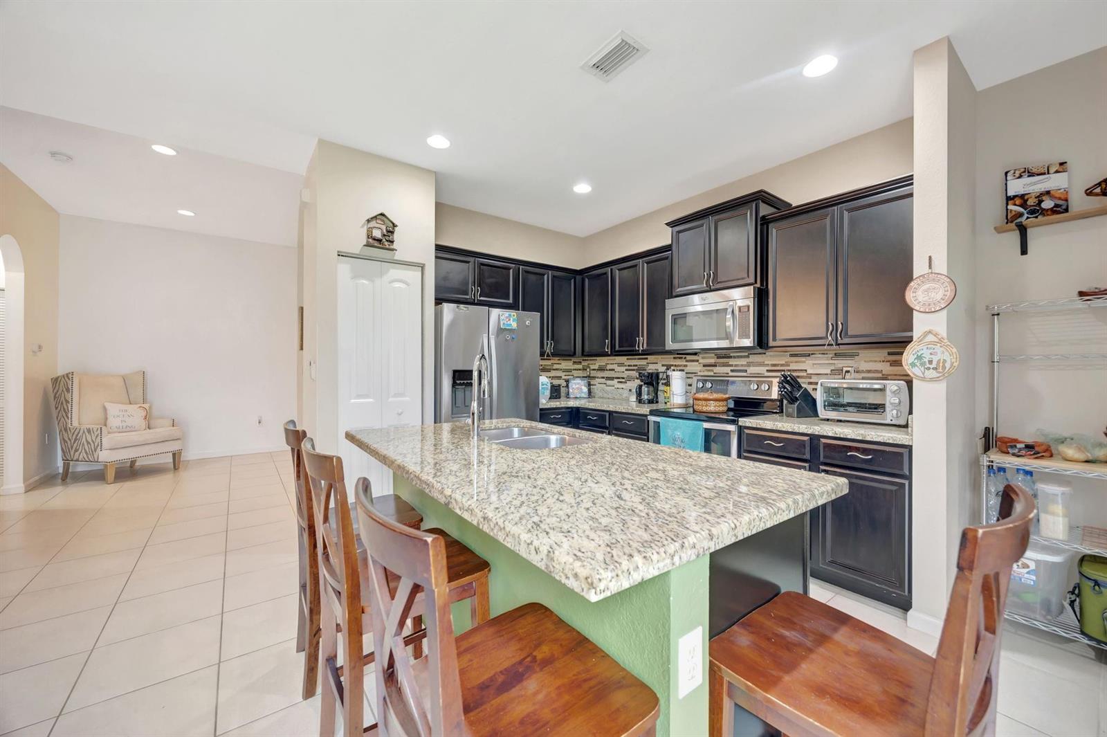 A kitchen features dark wood cabinets, granite countertops, a central island, and tile flooring — 25123 SW 118th Place, Cutler Bay FL 33032, CUTLER BAY, FL