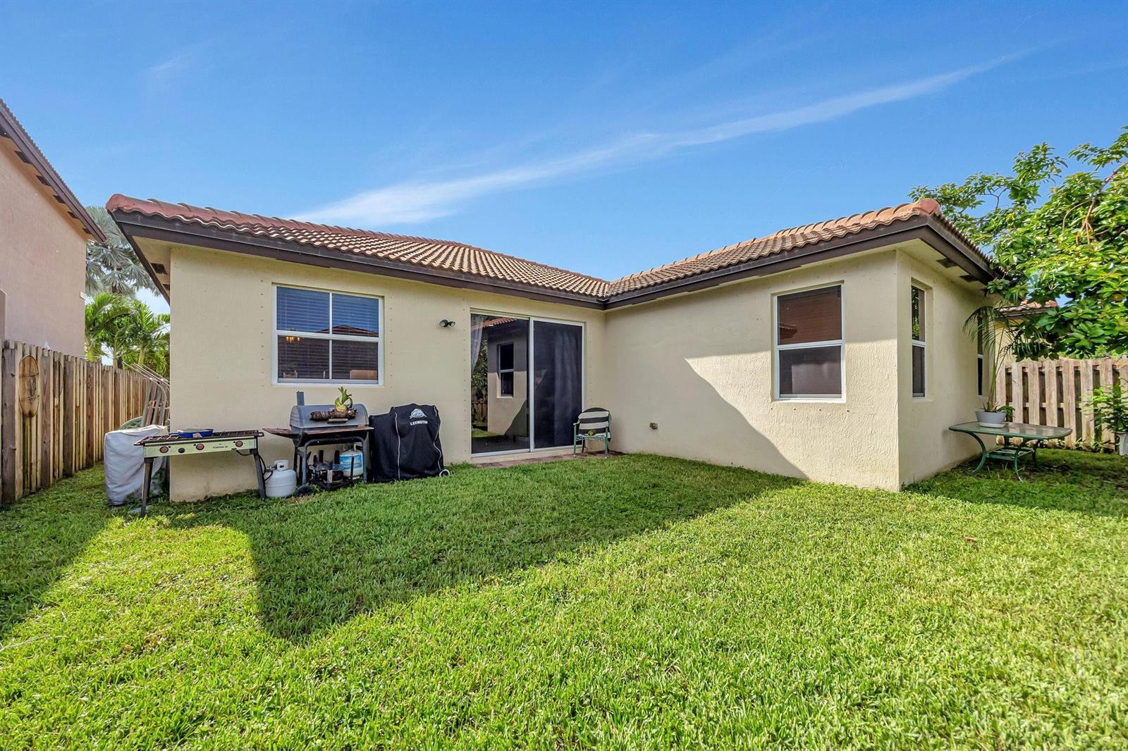 The exterior of a single-story house features a grassy backyard, sliding glass doors, and grills — 25123 SW 118th Place, Cutler Bay FL 33032, CUTLER BAY, FL