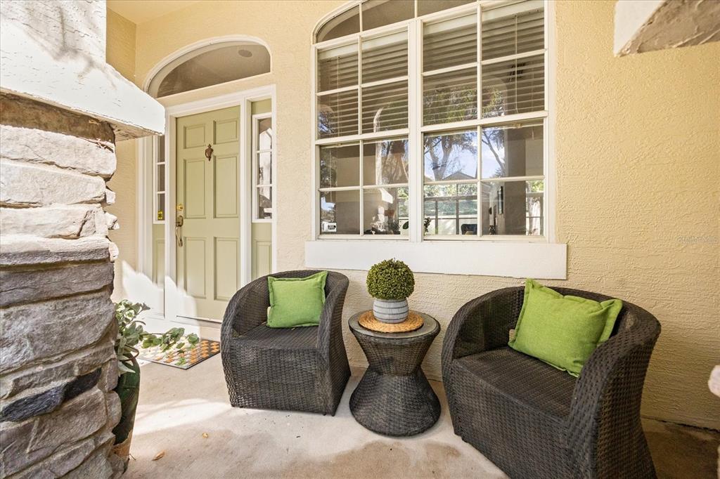 A covered front porch features two wicker chairs with green pillows and a small table — 220 WIMBLEDON CIRCLE, LAKE MARY, FL