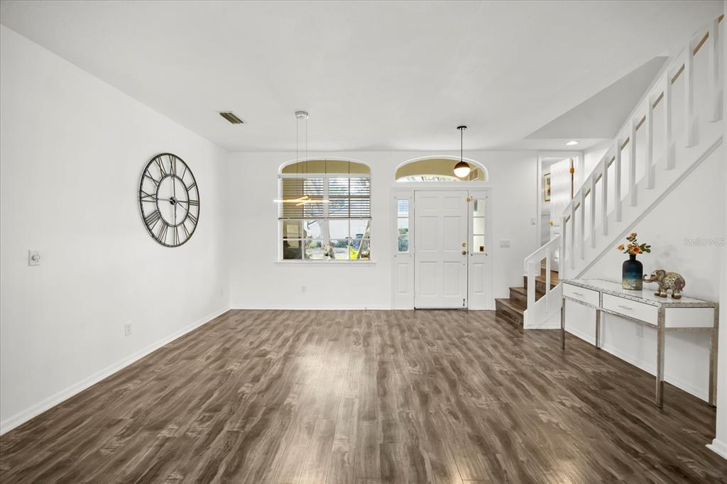 An entryway features wood-look flooring, a white staircase, a console table, and a large wall clock — 220 WIMBLEDON CIRCLE, LAKE MARY, FL