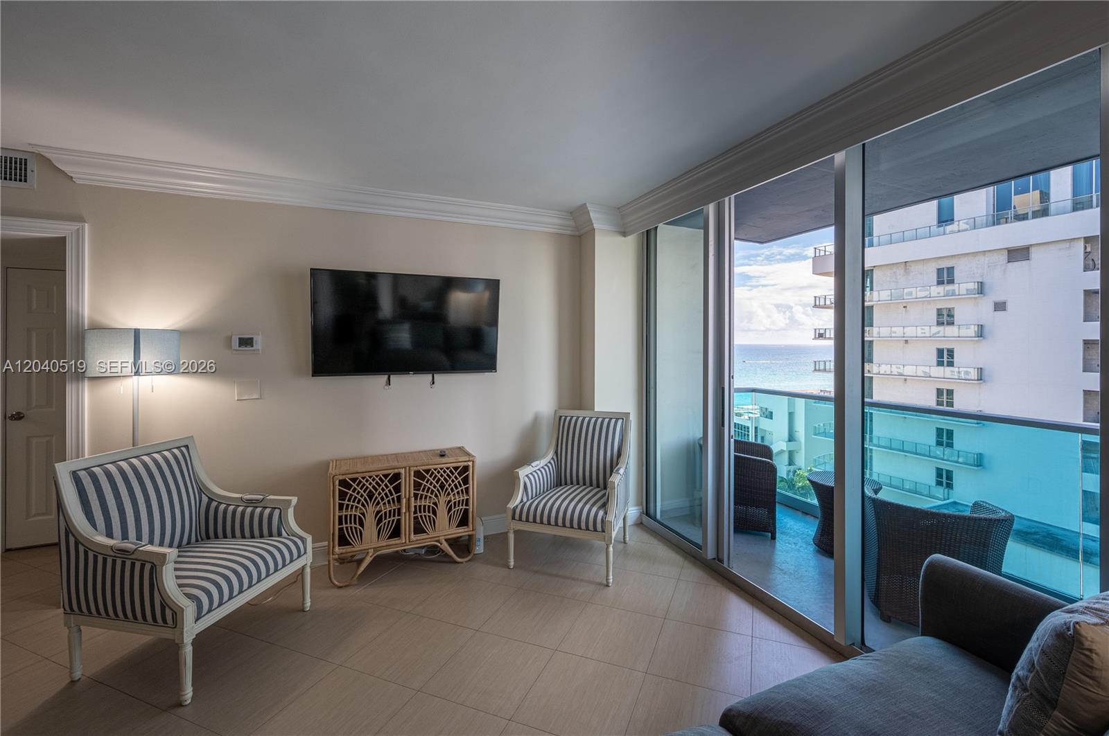 A living room features two striped chairs, a rattan console, and a balcony with ocean views — 4001 S Ocean Dr # 9J, Hollywood FL 33019, HOLLYWOOD, FL