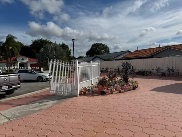 A white metal gate opens onto a paved driveway with potted plants and a car — 14365 SW 172nd Ln, Miami FL 33177, MIAMI, FL