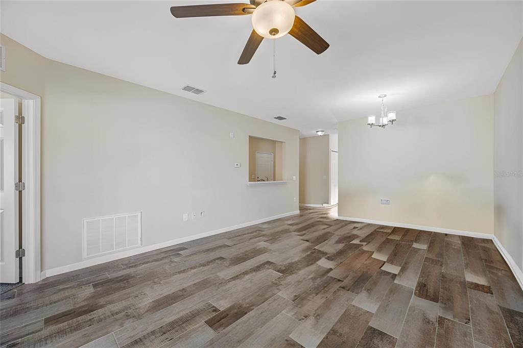 An open-concept living and dining area features wood-look tile flooring and a ceiling fan — 1195 GODAVARI WAY E UNIT 201, WESLEY CHAPEL, FL