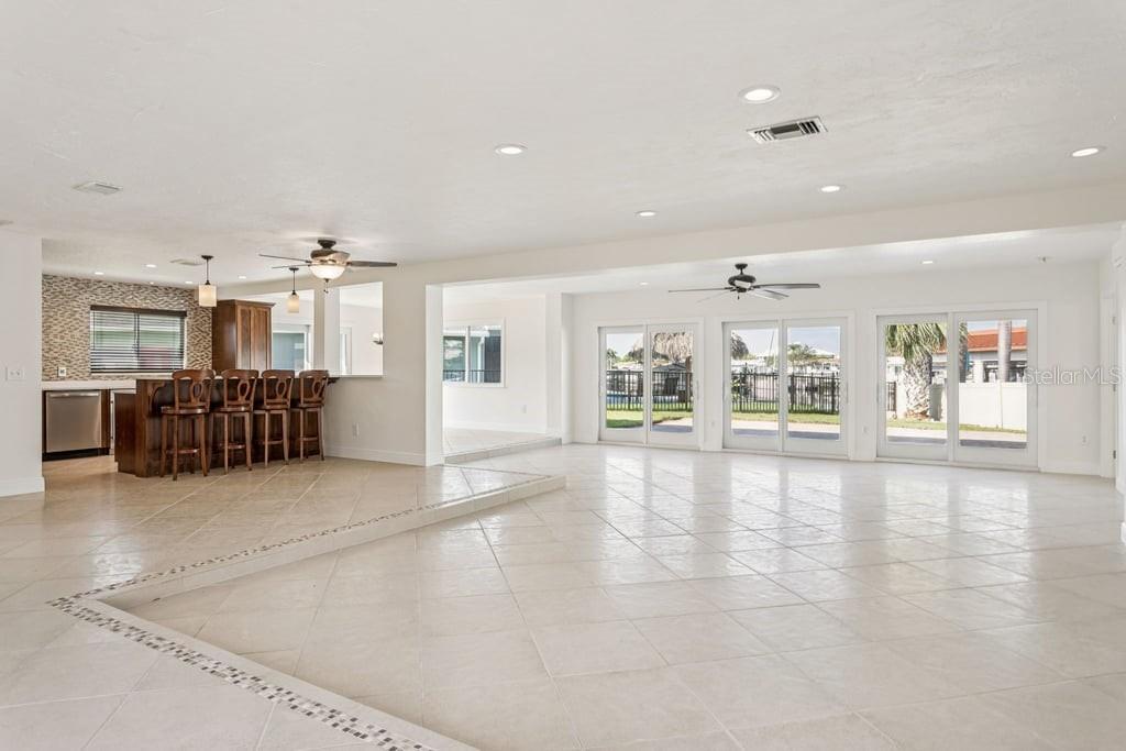 A spacious room with light tile floors, a kitchen island with bar seating, and sliding glass doors — 3734 TOPSAIL TRAIL, NEW PORT RICHEY, FL