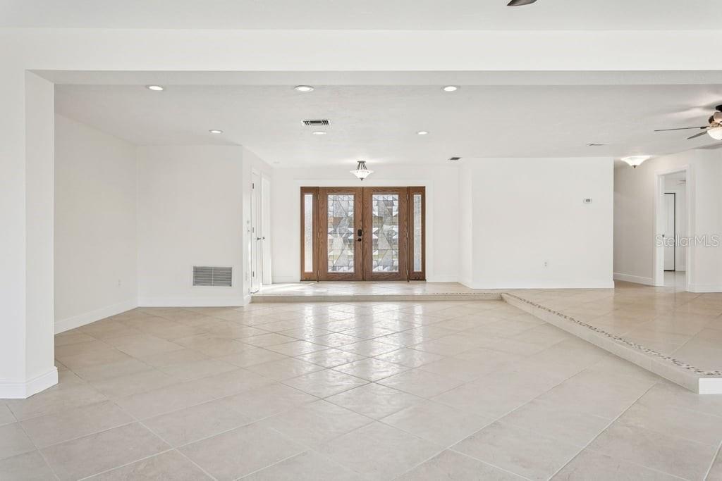 A spacious, white-walled foyer features large tile flooring, a sunken entryway, and decorative glass doors — 3734 TOPSAIL TRAIL, NEW PORT RICHEY, FL