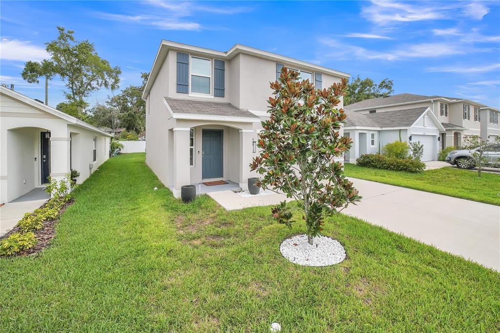 A two-story house with a beige stucco exterior, a gray front door, and a front lawn — 36558 SPANISH ROSE DRIVE, DADE CITY, FL