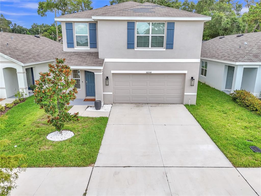 A two-story house with a beige stucco exterior, blue shutters, and a two-car garage — 36558 SPANISH ROSE DRIVE, DADE CITY, FL
