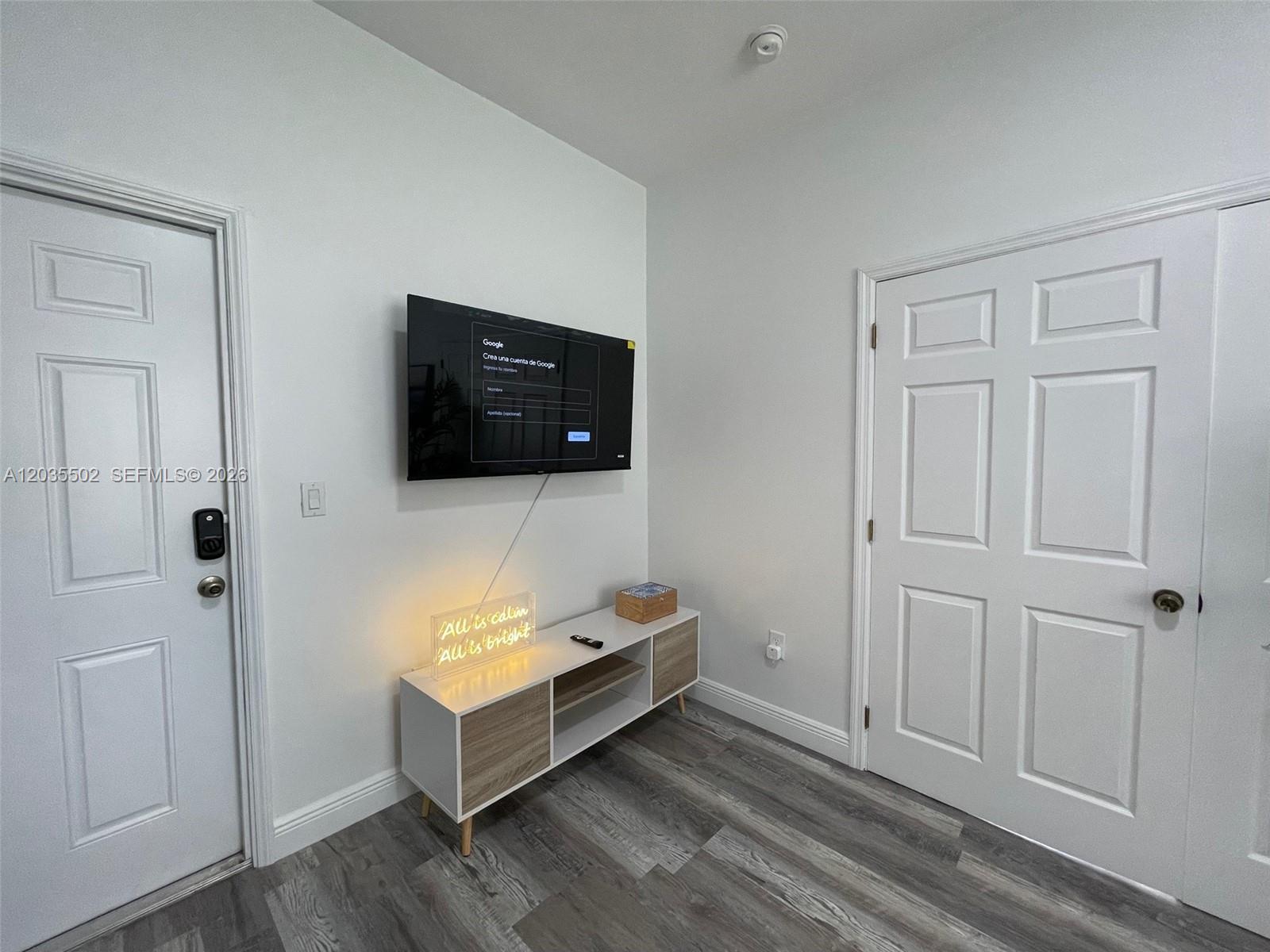 A room features a wall-mounted television, a media console, and two white doors on gray flooring — 29 Oviedo Ave # 1, Coral Gables FL 33134, CORAL GABLES, FL