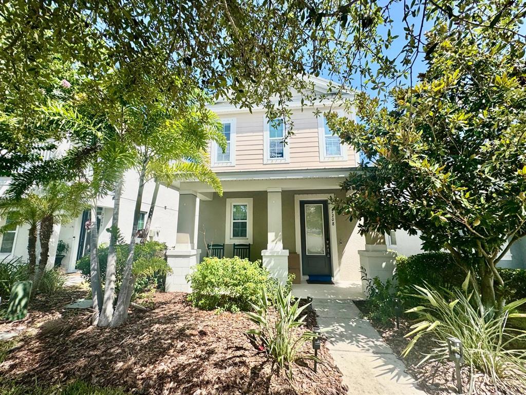 A two-story house with light-colored siding, a front porch, and a walkway surrounded by landscaping — 7208 MILESTONE DRIVE, APOLLO BEACH, FL